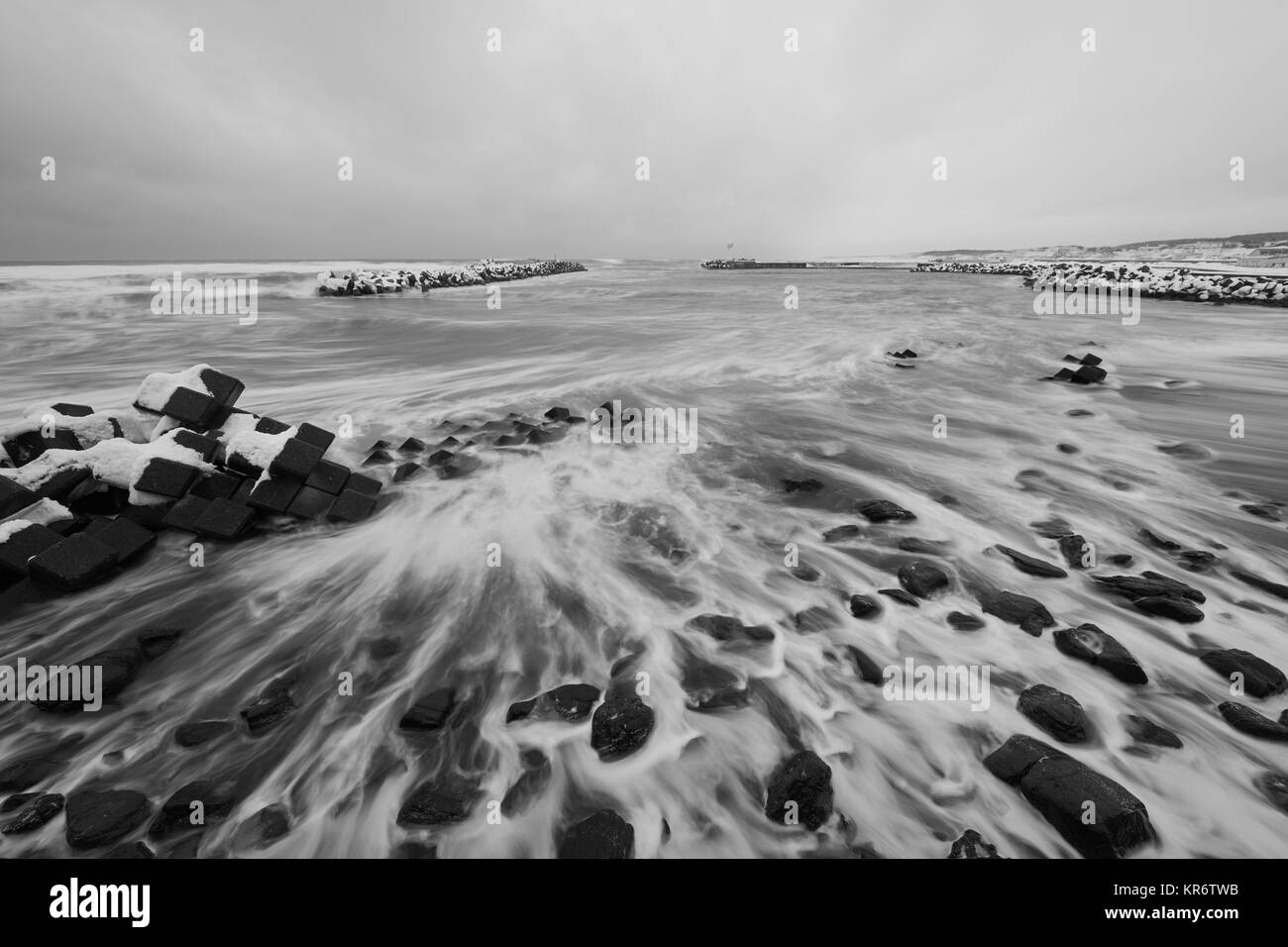 Verschneite Wellenbrecher auf einem felsigen Strand im Winter. Stockfoto