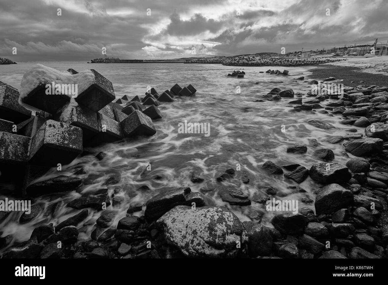 Verschneite Wellenbrecher auf einem felsigen Strand im Winter. Stockfoto