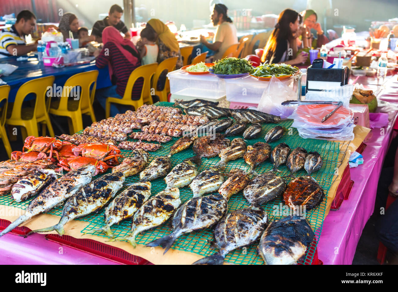Hohe Betrachtungswinkel von gegrilltem Fisch auf einem Tisch in einem Lebensmittelmarkt Restaurant, Menschen sitzen und essen an den Tischen in den Hintergrund. Stockfoto