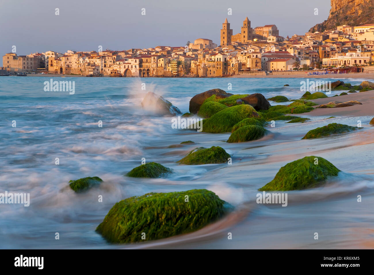 Blick entlang der Küste mit Sandstrand, Felsen, mit grünen Algen, die Stadt in der Ferne. Stockfoto