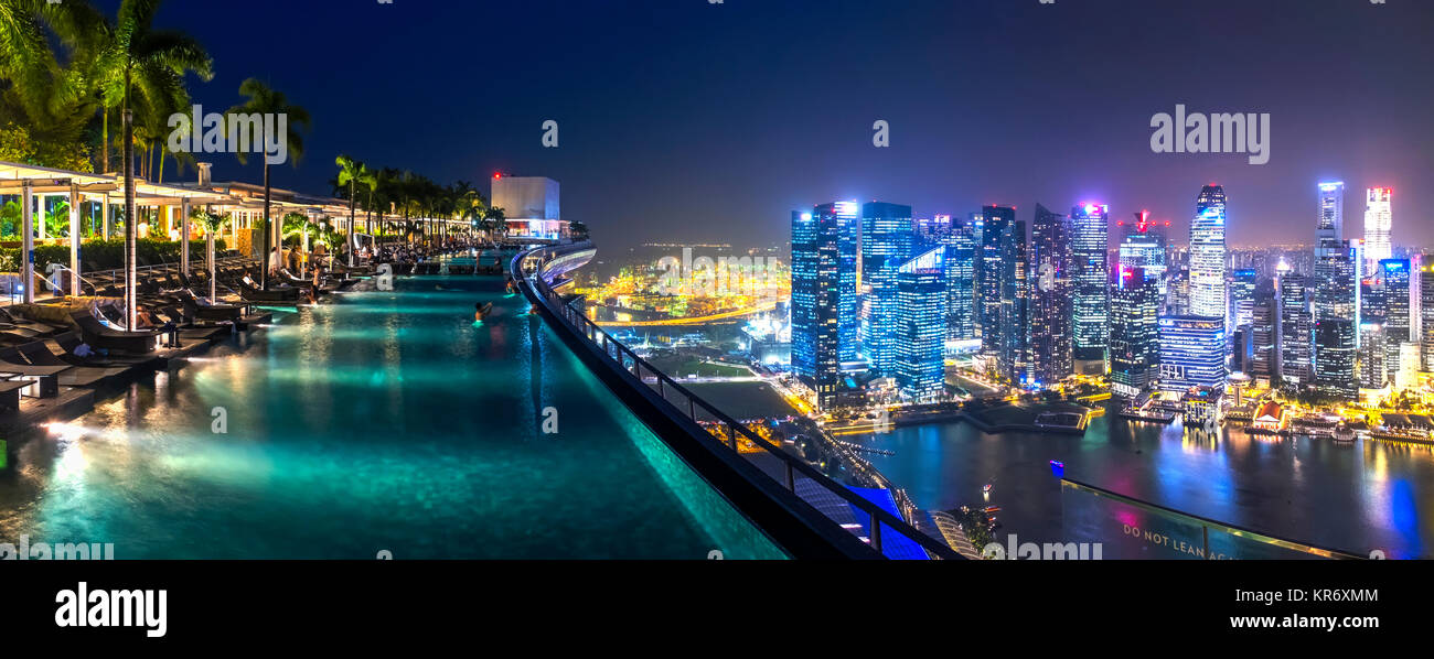 Abendlicher Blick entlang der beleuchteten Infinity Pool auf der Dachterrasse, Stadtbild mit Wolkenkratzern in der Ferne. Stockfoto