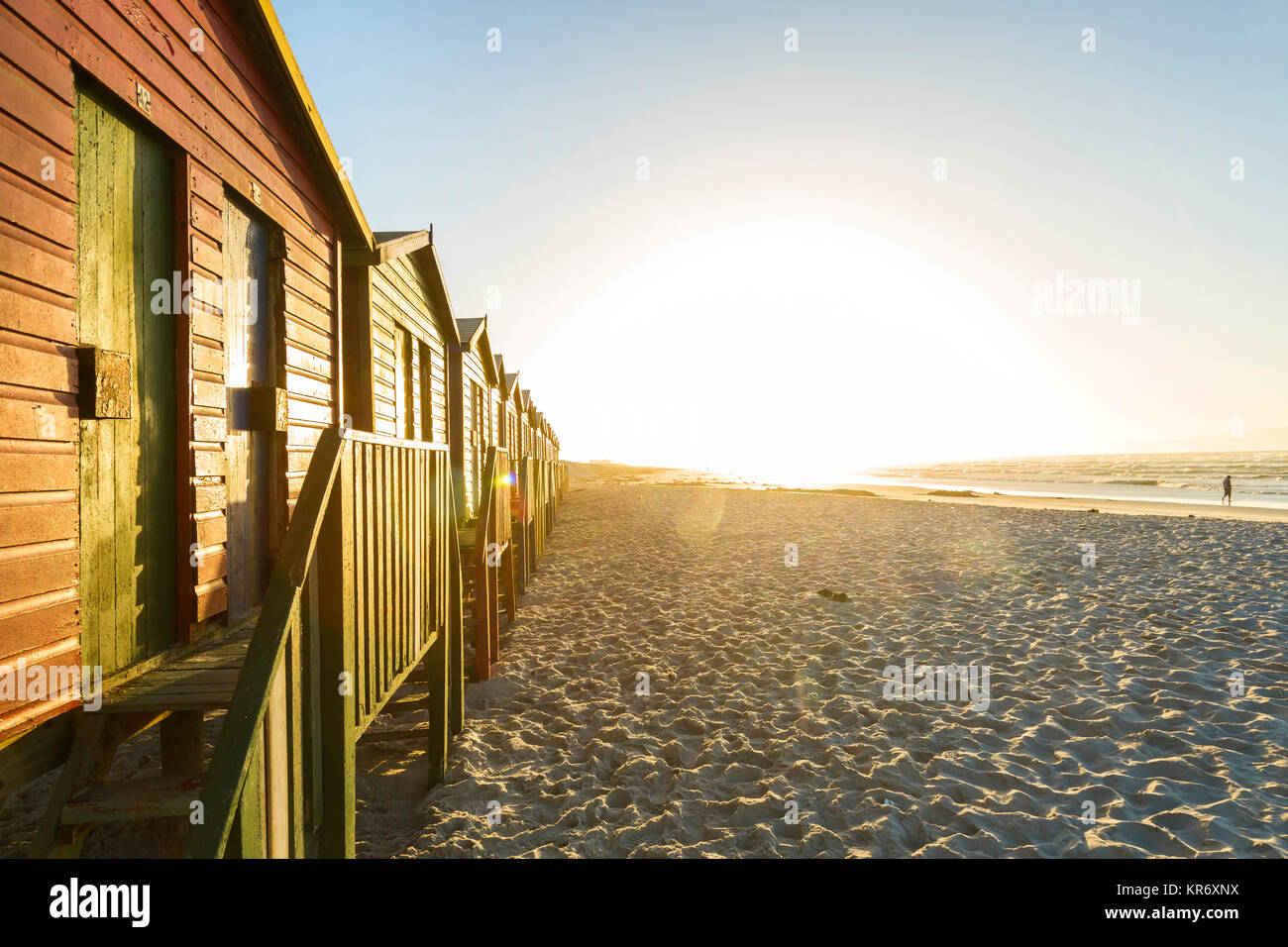 Blick entlang einer Reihe von bunten hölzernen Umkleidekabinen am Strand an einem langen Sandstrand bei Sonnenaufgang. Stockfoto