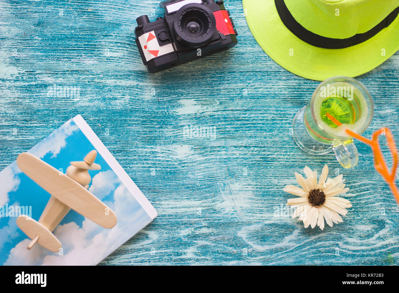 Urlaub - genießen Sie einen tropischen Cocktail, eine Rolle Film vintage Kamera, ein hölzernes Spielzeug Flugzeug und einem hellen grünen Hut auf einem blauen Hintergrund aus Holz. Platz für ein Stockfoto