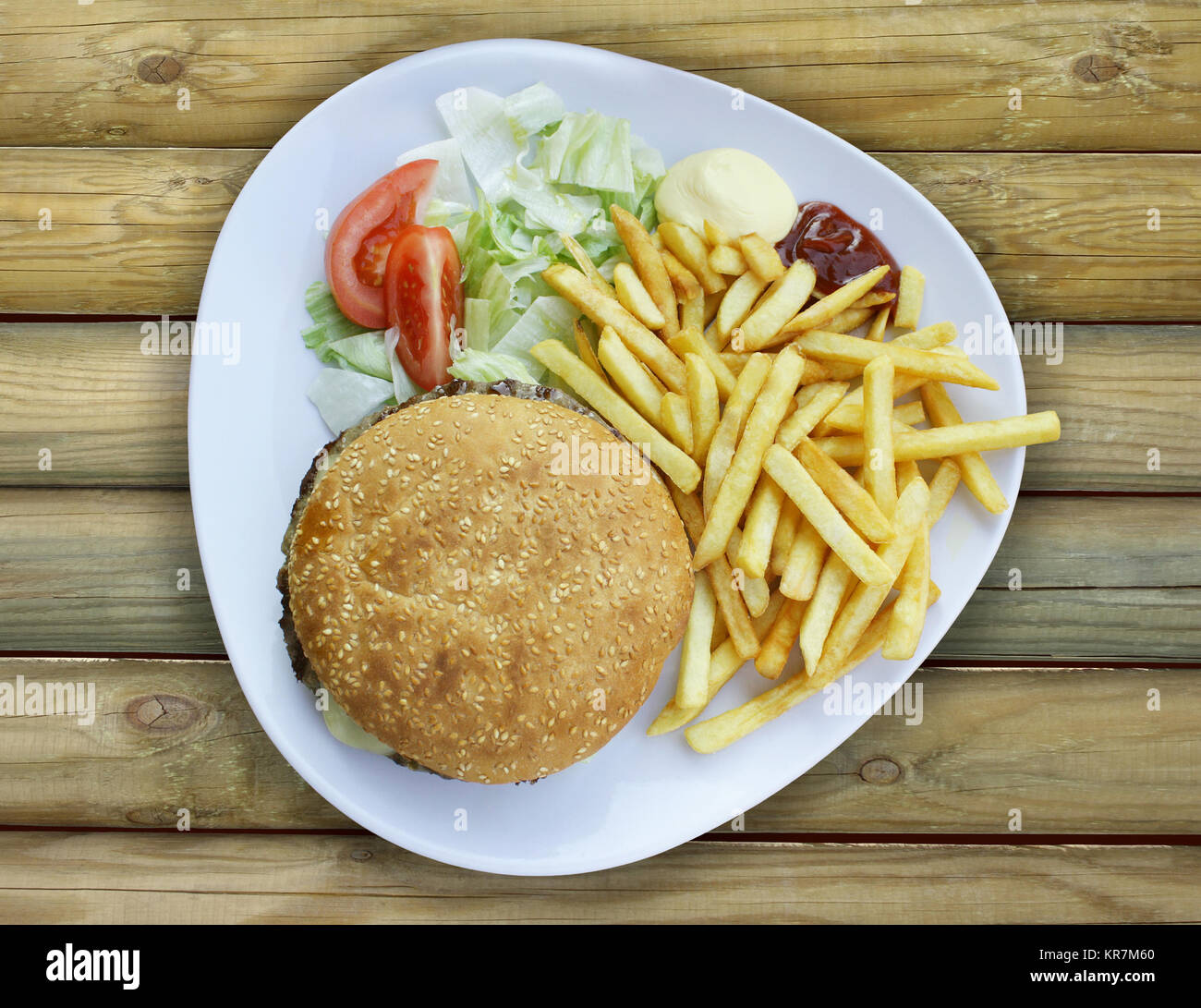 Foto von oben auf eine Platte mit Cheeseburger, Pommes und Soßen auf einem Holztisch Stockfoto