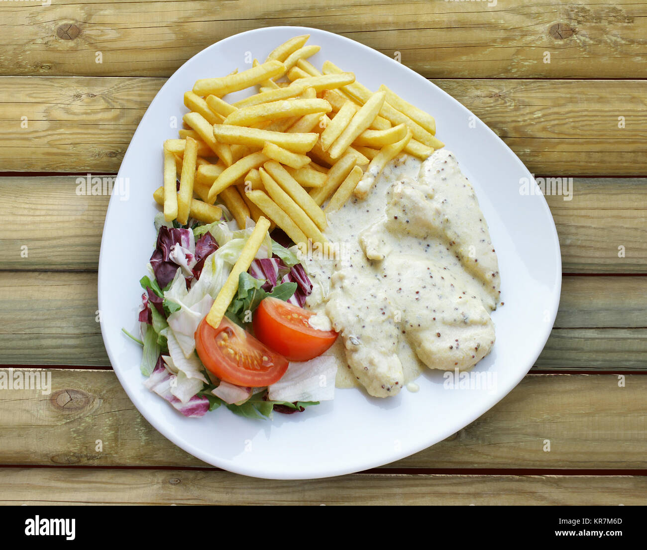 Foto von oben, eine Platte mit aromatischen Hähnchen mit Pommes und gemischtem Salat auf einem Holztisch Stockfoto
