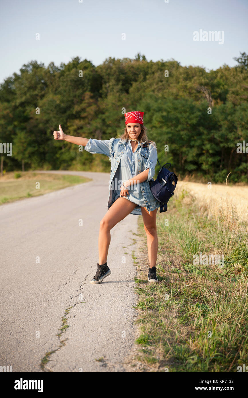 Junge Frau per Anhalter Fahren auf einer Landstraße Stockfoto