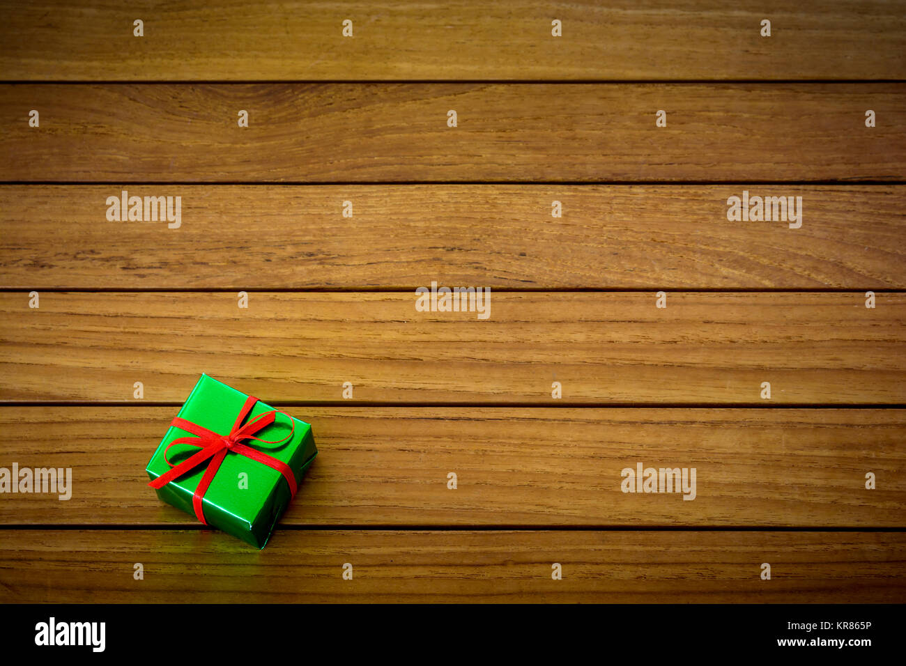 Metallic grün Geschenk Paket mit roter Schleife auf einer hölzernen Hintergrund. Stockfoto