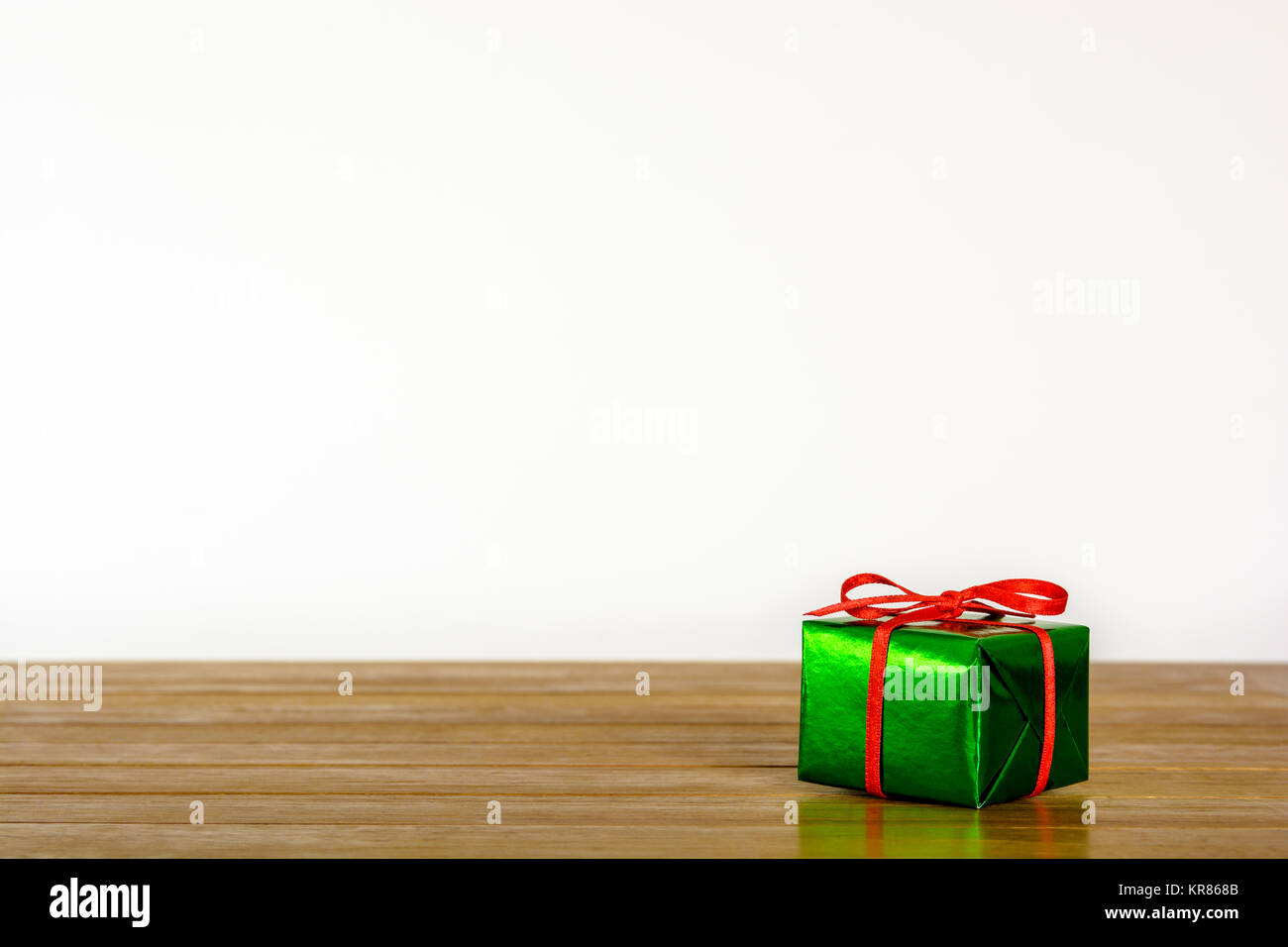 Metallic grün Geschenk Paket mit roter Schleife auf einem holztisch vor einem weißen Hintergrund. Stockfoto