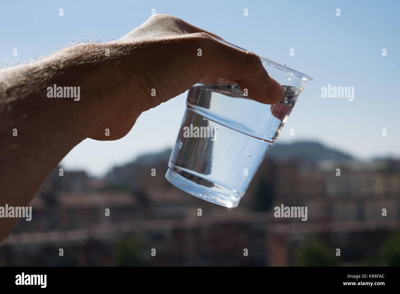 Eine schräge Glas Wasser in der Hand mit dem städtischen defokussiertem Hintergrund. Stockfoto
