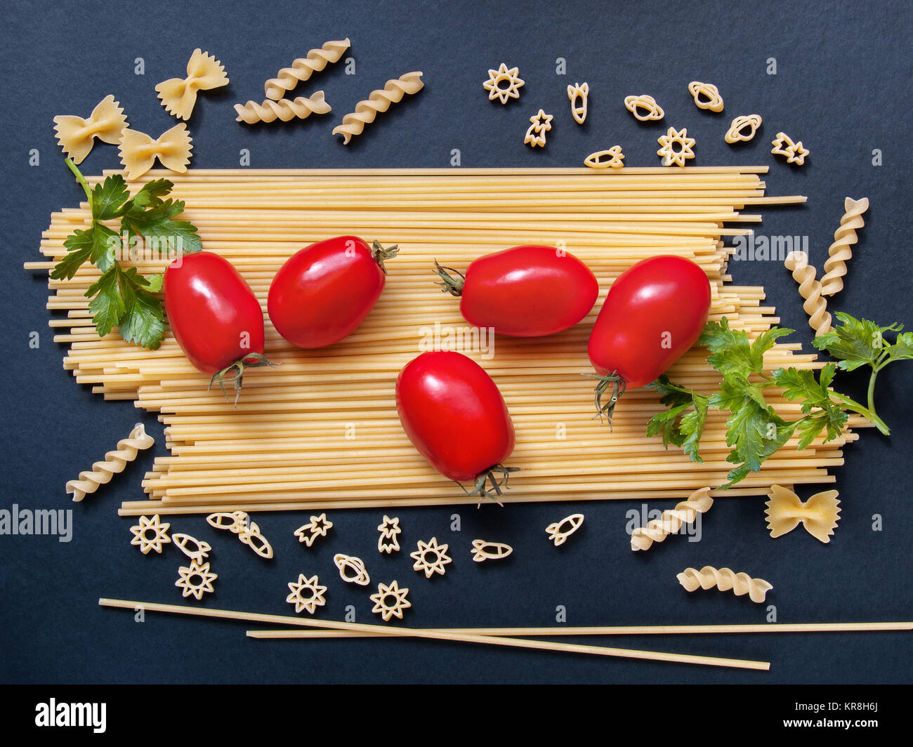 Spaghetti mit Tomaten, Grünen und andere dar, Nudeln in Form von Bögen, Spiralen, Zahlen von Raketen und Sterne für Kochen auf einem dunklen Hintergrund Stockfoto