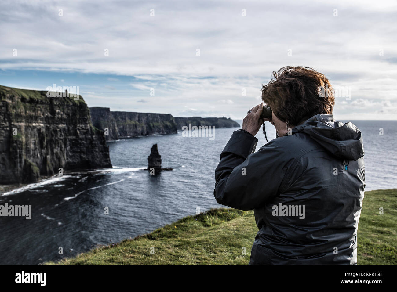 Irland, Clare County, Frau suchen durch ein Fernglas auf den Klippen von Moher Stockfoto