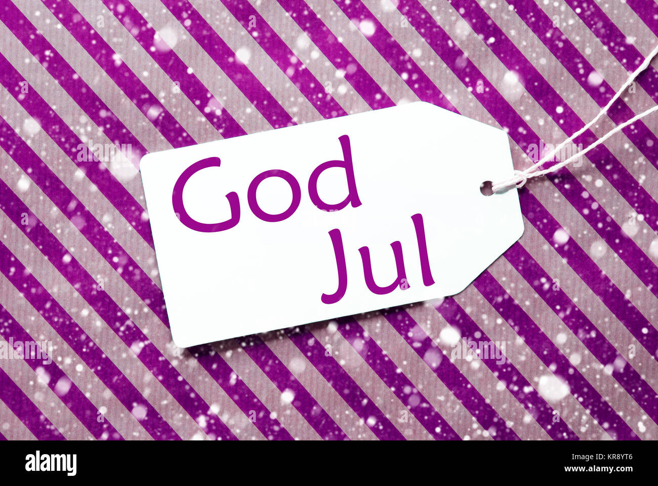 Ein Etikett auf lila gestreiften Verpackung Papier. Strukturierten Hintergrund mit Schneeflocken. Tag mit Band. Schwedische Text Gott Aug bedeutet Frohe Weihnachten Stockfoto