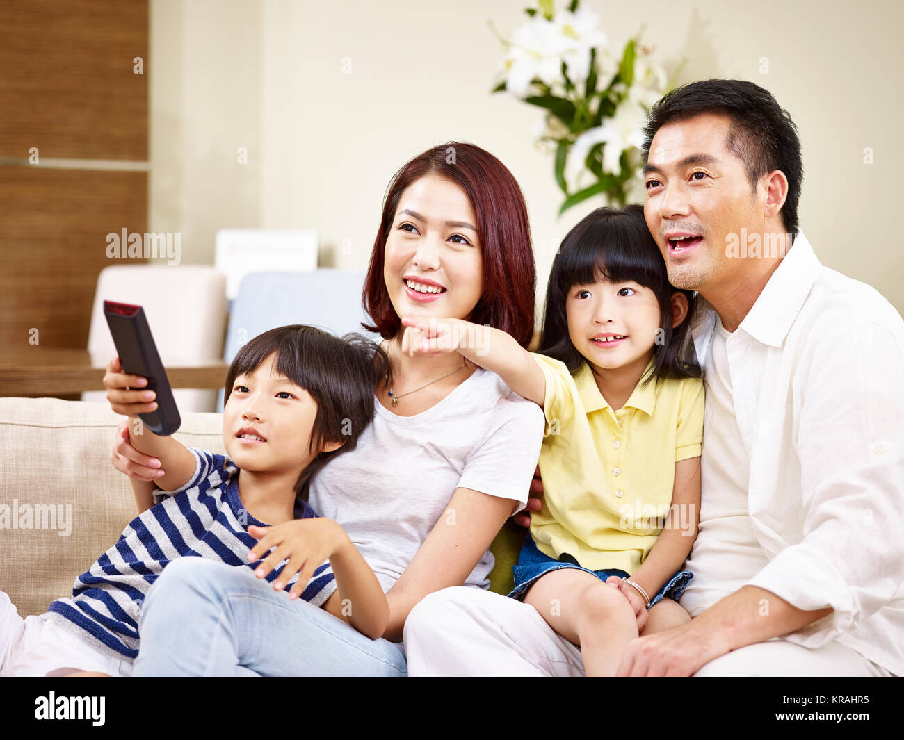 Asiatische Familie mit zwei Kindern sitzt auf der Couch zu Hause vor dem Fernseher. Stockfoto