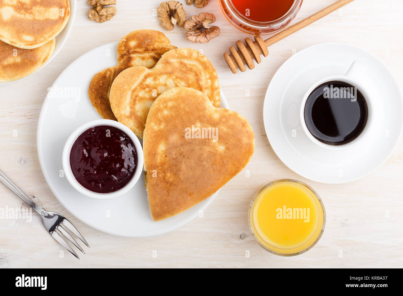 Valentinstag Frühstück oder Brunch. Hausgemachte Herzform Pfannkuchen mit Beeren Marmelade und Honig, Orangensaft und Kaffee. Tabelle gesehen von oben Stockfoto