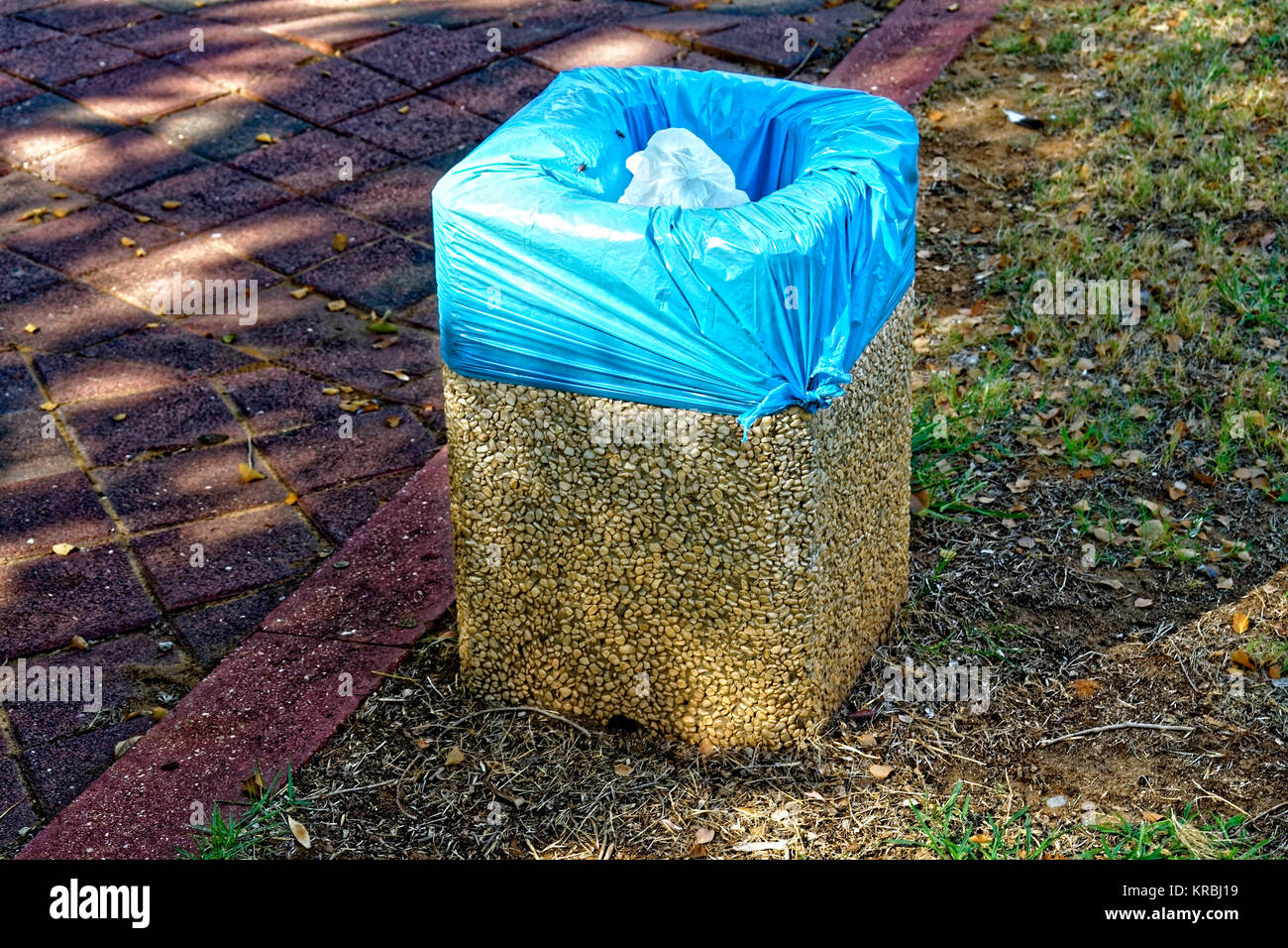 Kleine Steine Papierkorb mit einem blauen Müllsack die Steine sind wahrscheinlich zusammen durch Zement statt sie sehen eine weiße Plastiktüte in den Papierkorb. Stockfoto