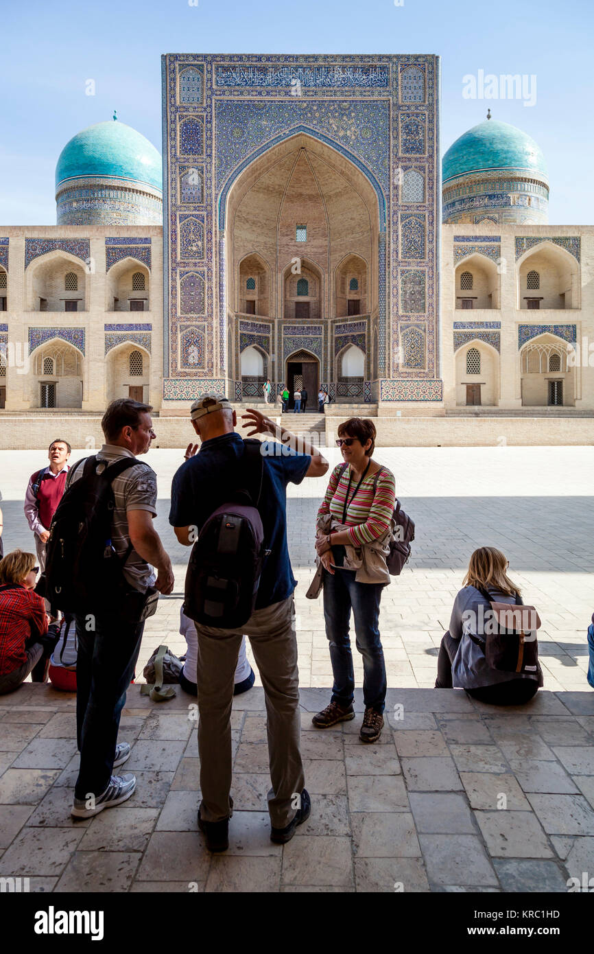 Eine Gruppe von Touristen, die sich in der POI KALYAN mit der Mir-i-arabischen Madrassa im Hintergrund, Buchara, Usbekistan Stockfoto