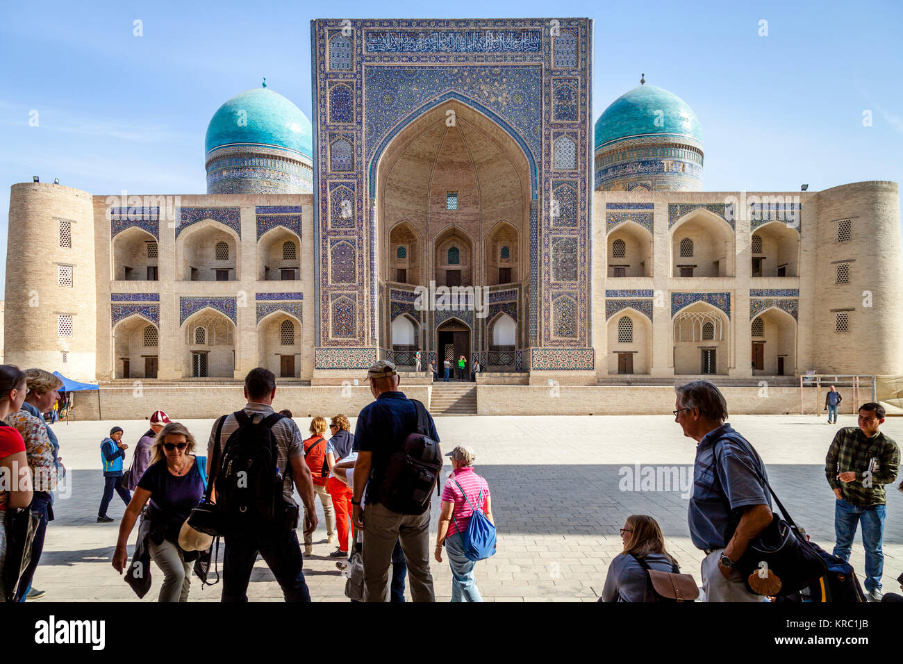 Eine Gruppe von Touristen, die sich in der POI KALYAN mit der Mir-i-arabischen Madrassa im Hintergrund, Buchara, Usbekistan Stockfoto