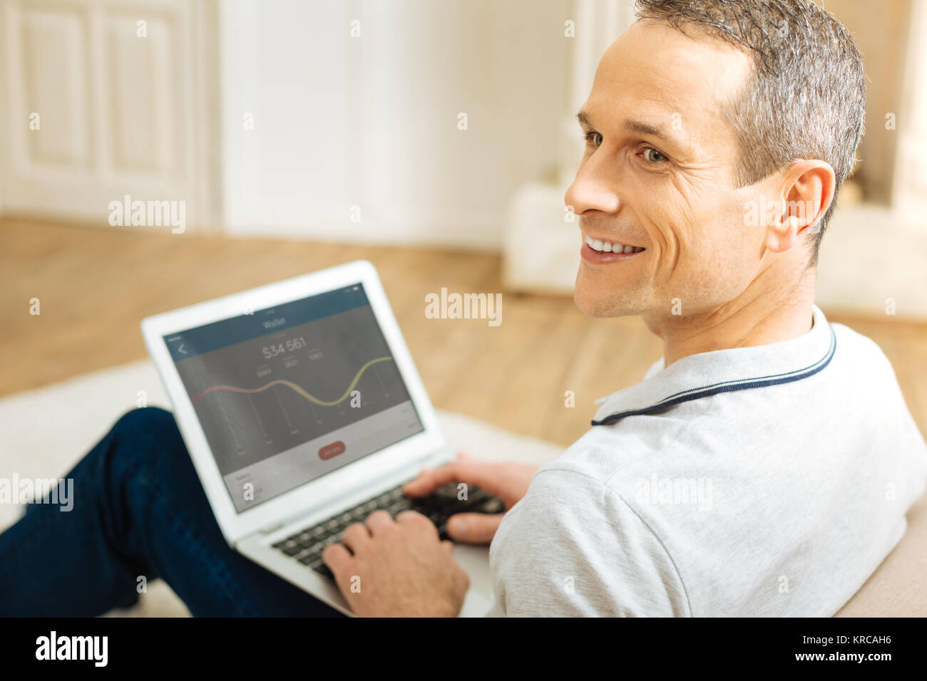 Positive zuversichtlich Mann lächelnd, während das Arbeiten zu Hause auf seinem Laptop Stockfoto