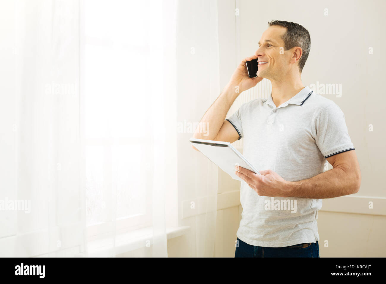 Glücklich lächelnde Mann am Telefon zu sprechen, während sie in das Fenster suchen Stockfoto