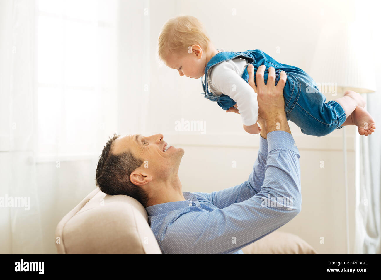 Freundliche Vater, der sein Baby in die Luft und glücklich lächelnd begeistert Stockfoto