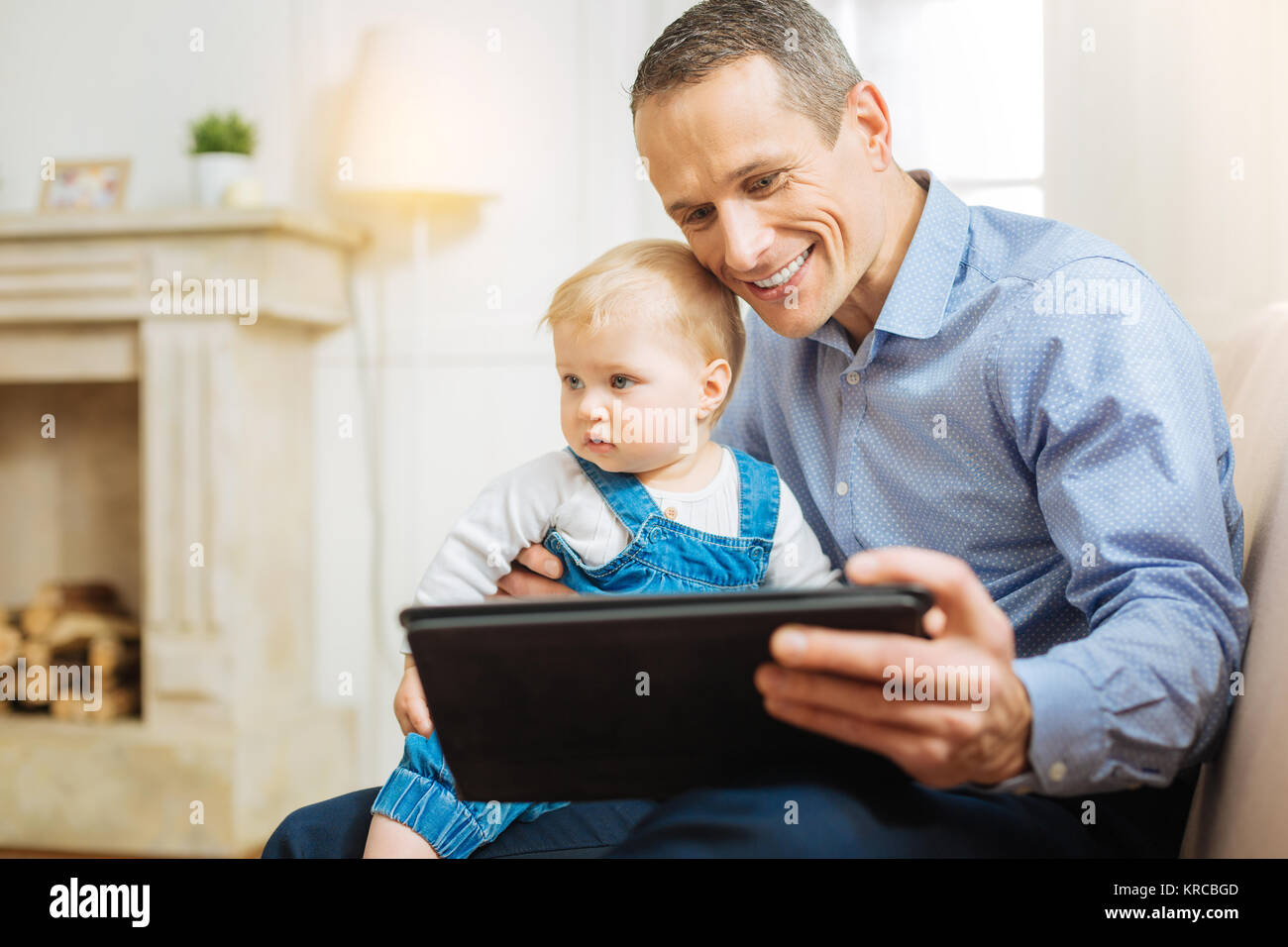 Glückliche junge Mann lächelnd während der Sitzung mit einem Baby und einem Tablet Stockfoto