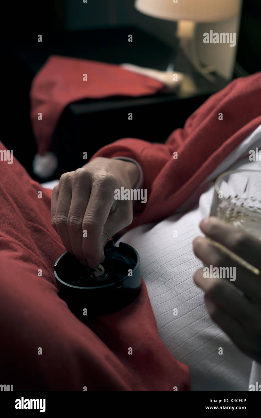 Nahaufnahme von einem jungen Mann, der eine Santa Anzug Whisky trinken und rauchen eine Zigarette im Bett Stockfoto