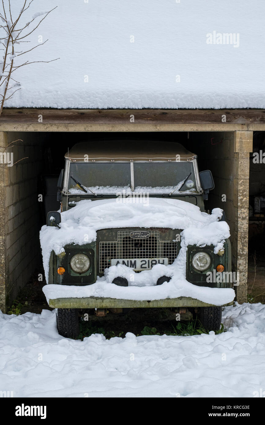 Jahrgang 1969 Land Rover abgedeckt im Schnee in eine offene Garage geparkt. Chedworth, Cotswolds, Gloucestershire, England Stockfoto