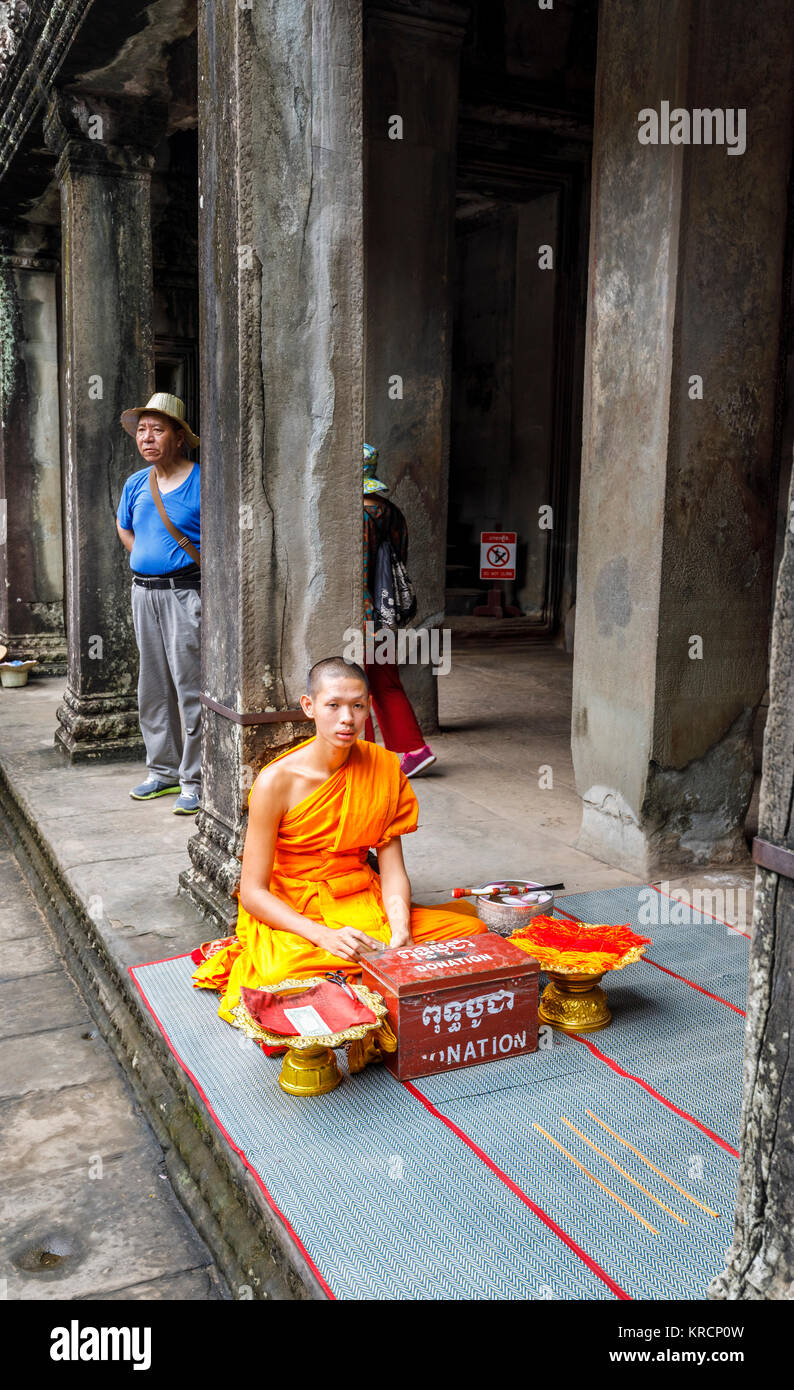 Junger buddhistischer Mönch in Safranroben sitzt in Angkor Wat, eine Tempelanlage in der Nähe von Siem Reap in Kambodscha, das größte religiöse Monument der Welt Stockfoto