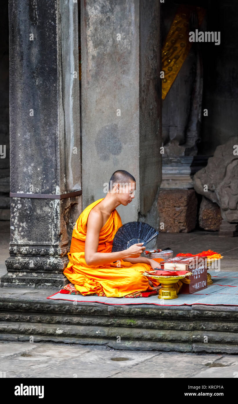 Junger buddhistischer Mönch in Safranroben sitzt in Angkor Wat, eine Tempelanlage in der Nähe von Siem Reap in Kambodscha, das größte religiöse Monument der Welt Stockfoto