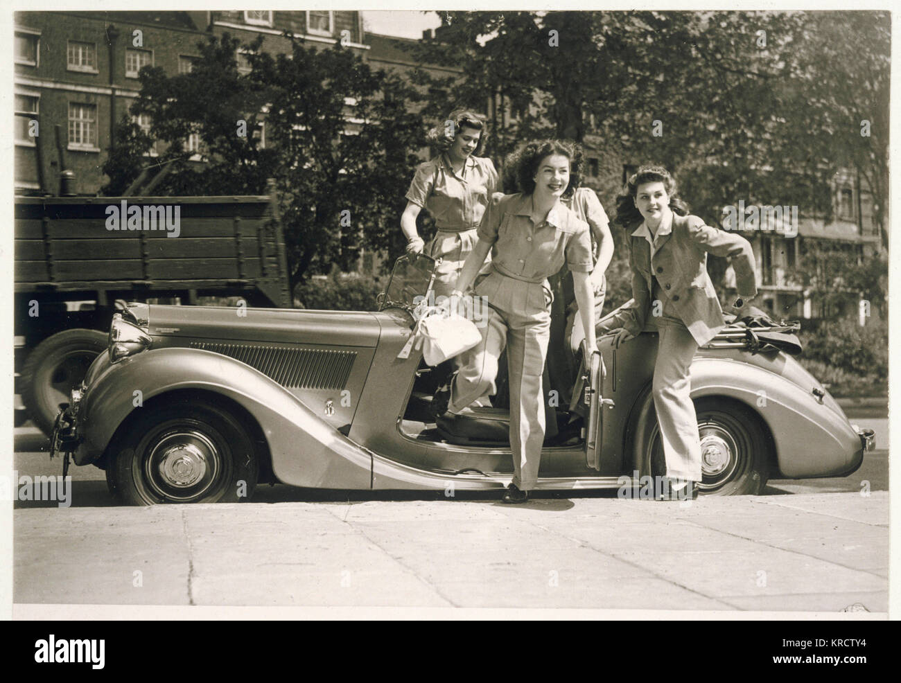 Vier bezaubernde Krieg - Zeit Frauen in hosenanzügen mit breiten Beinen Hose, Shirt Style Blusen &Amp; Jacken mit Schulterpolstern Sprung aus einem oben offenen Auto. Termin: Anfang 1940 s Stockfoto