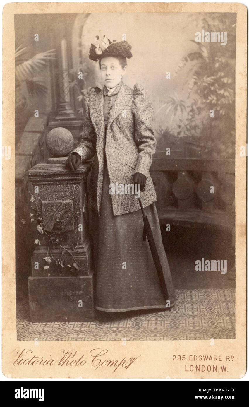 Eine junge Frau in ihrem viktorianischen Outdoor Kleidung posiert im Studio des Fotografen. Sie hält einen gerollten Regenschirm in der einen Hand und lehnte sich auf einer steinernen Balustrade. Datum: ca. 1890 s Stockfoto