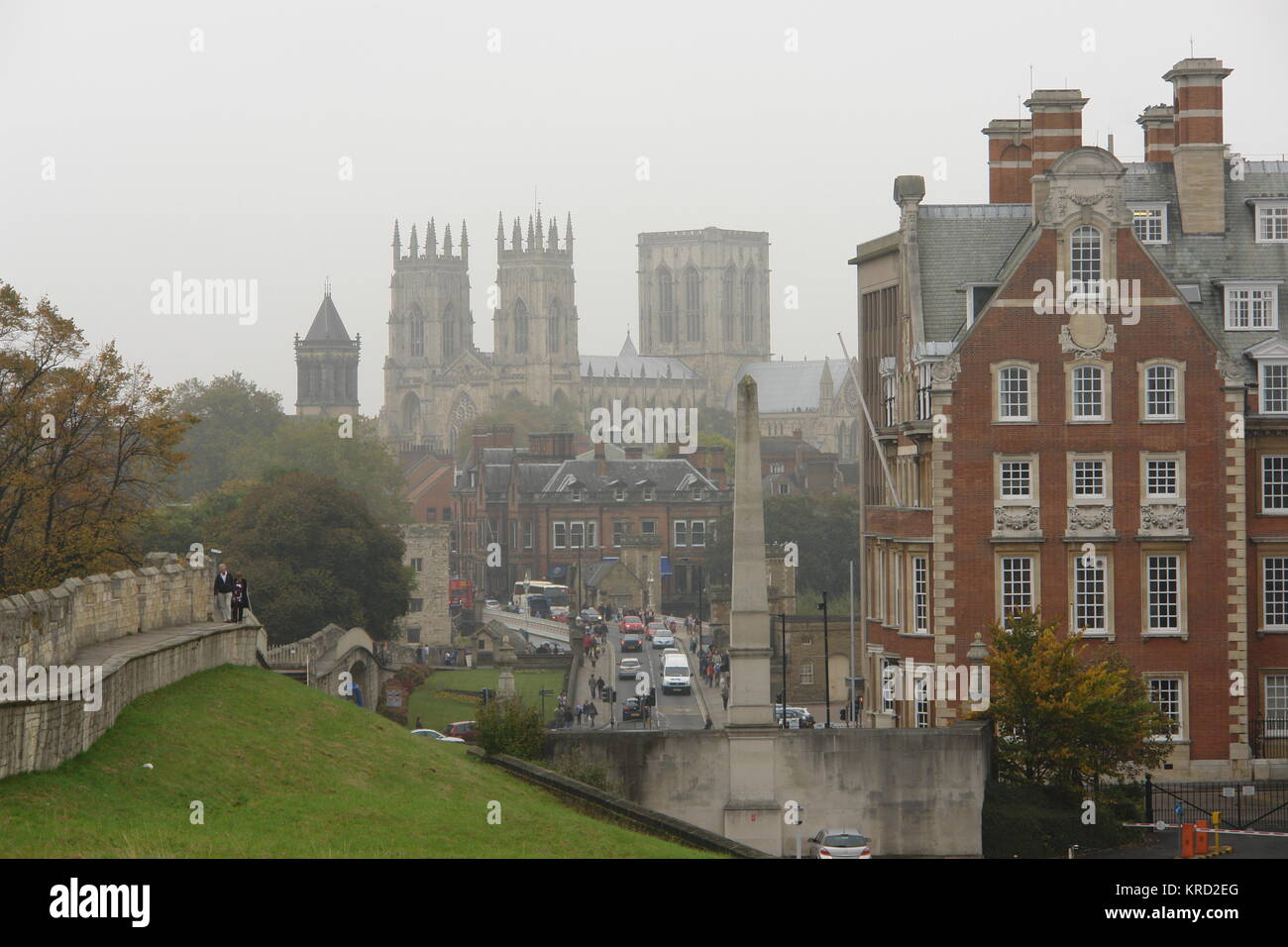 Blick auf das York Minster an einem grauen Tag. Das Gebäude begann 1220 -- es ist eine der größten gotischen Kathedralen in Nordeuropa und ist der Sitz des Erzbischofs von York. Man kann auf der linken Seite Menschen sehen, die entlang der alten Stadtmauern spazieren. Stockfoto