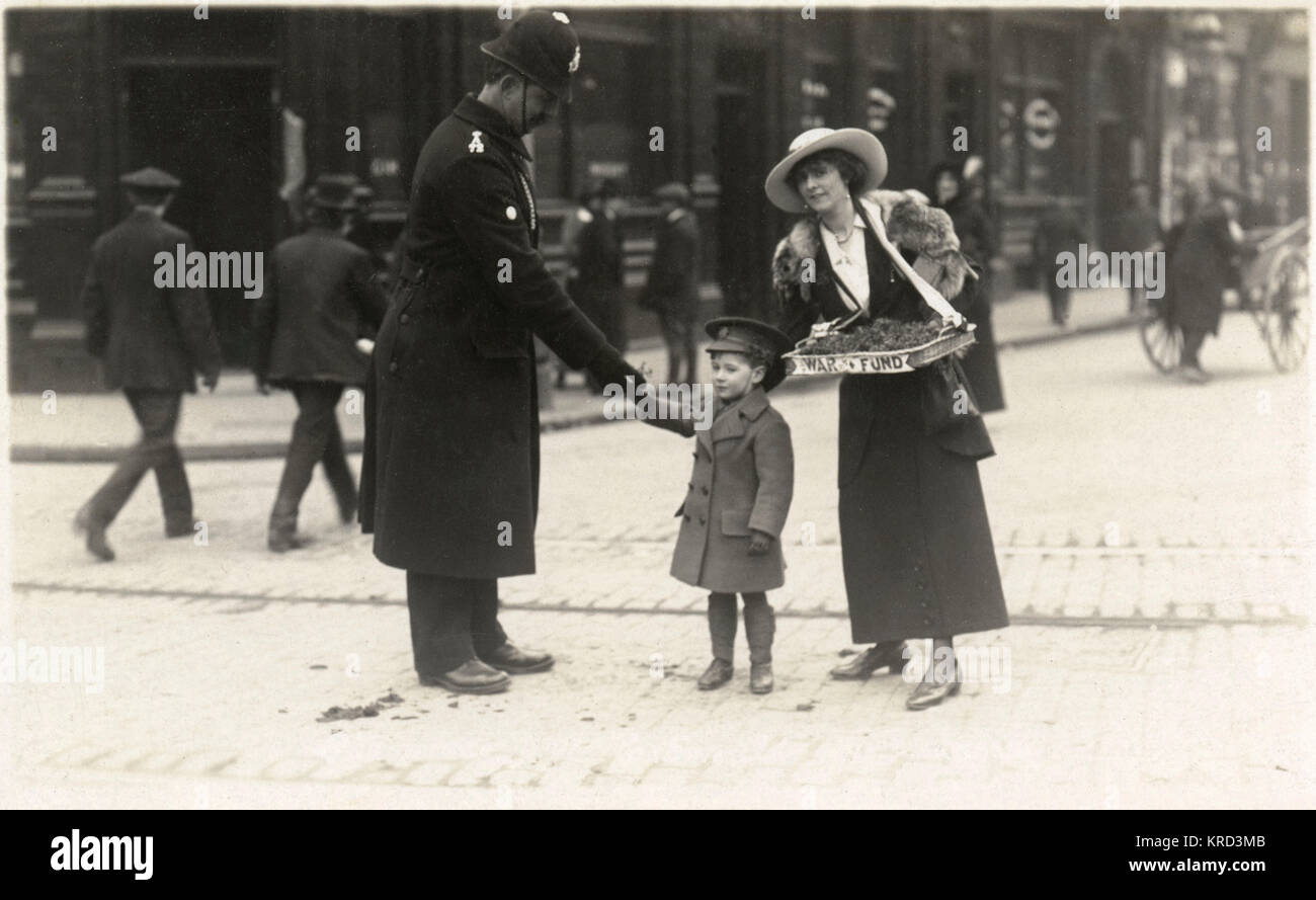 Ein kleiner Junge, gekleidet in Uniform eines Miniatur britischer Offizier verkauft ein Flag, das eine verbindliche Polizeioffizier mit Hilfe einer Frau, die vermutlich seine Mutter. Während des Großen Krieges um Großbritannien, es gab zahlreiche Flagge Tage, mit Damen (und Kinder) Verkauf von Fahnen Mittel für verschiedene Krieg Nächstenliebe zu heben. c. 1915 Stockfoto