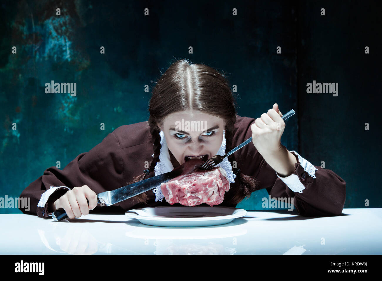 Blutige Halloween-Thema: Verrücktes Mädchen mit Messer, Gabel und Fleisch Stockfoto
