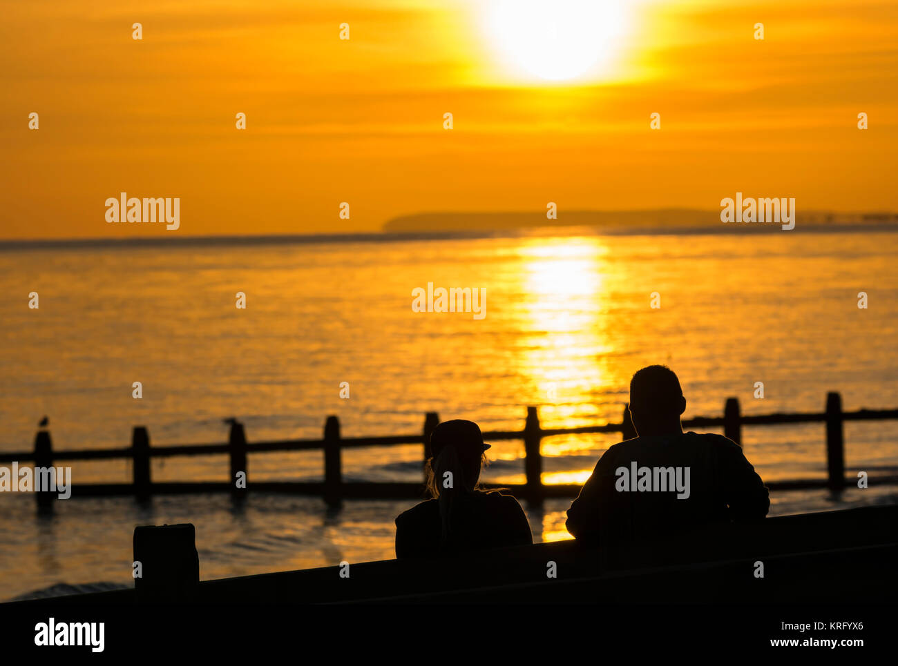 Paar am Strand beobachten, wie die Sonne über dem Meer, in Großbritannien. Stockfoto