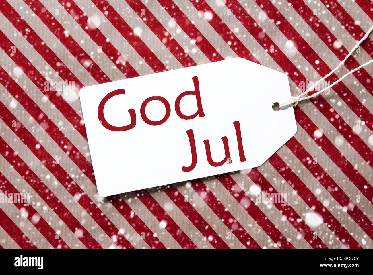 Ein Etikett auf einer rot-braun gestreiften Verpackung Papier. Strukturierten Hintergrund mit Schneeflocken. Tag mit Band. Schwedische Text Gott Aug bedeutet Frohe Weihnachten Stockfoto