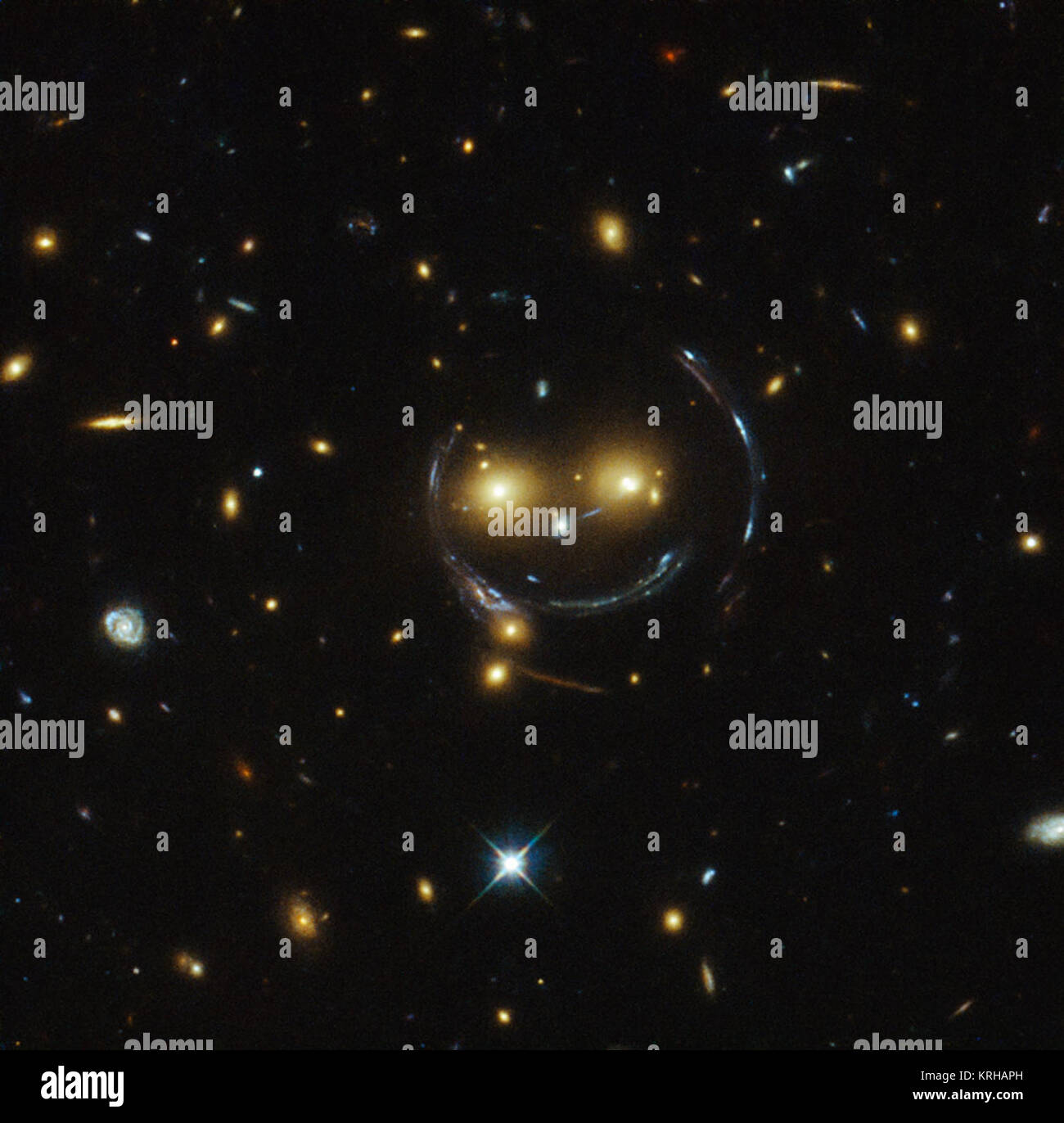 In der Mitte dieses Bild, mit dem Hubble-Weltraumteleskop der NASA/ESA, ist das Galaxy cluster SDSS J 1038 +4849 - und es scheint zu lächeln. Sie können die beiden orangefarbenen Augen und weißen Knopf Nase heraus. Im Falle dieses "Happy Face", die beiden Augen sind sehr hellen Galaxien und die irreführende Lächeln Linien sind tatsächlich Bögen durch einen Effekt so stark Gravitationslinseneffekts verursacht. Galaxienhaufen sind die massiven Strukturen im Universum und diese üben eine starke Anziehungskraft, dass sie die Raumzeit verzerren um Sie herum und als kosmische Linsen, die vergrößern kann, Verdrehen und Verbiegen der Stockfoto