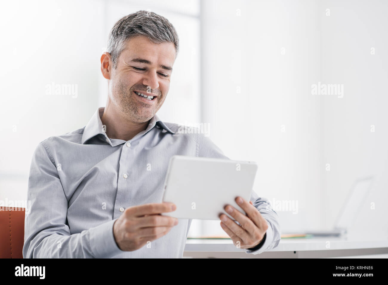 Lächelnd zuversichtlich Geschäftsmann mit einem Touchscreen Tablet-PC im Büro, er ist ein Video ansehen und genießen Stockfoto