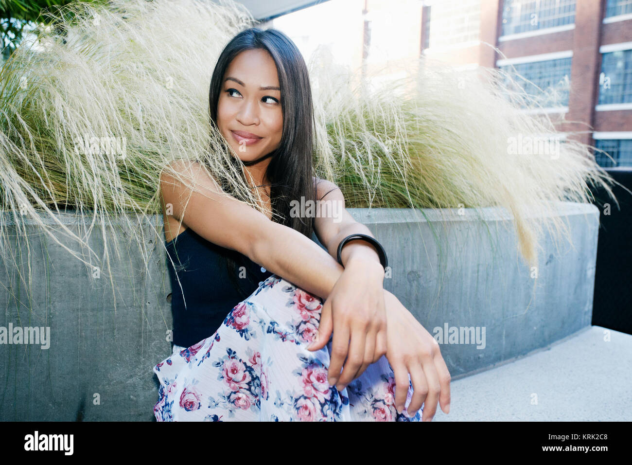 Lächelnd asiatische Frau sitzt in der Nähe von Laub Stockfoto