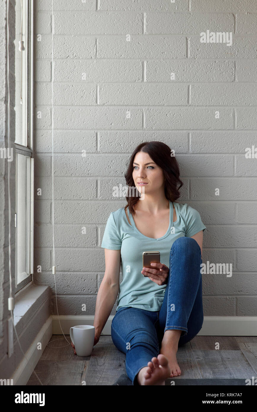 Kaukasische Frau sitzt auf dem Boden von SMS auf Handy Stockfoto