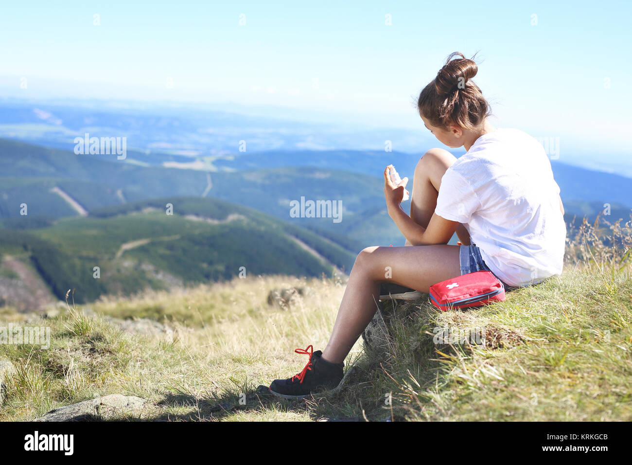 Touristische desinfiziert die Wunde an seinem Knie beim Sitzen auf dem Hang eines Berges Trail. Stockfoto