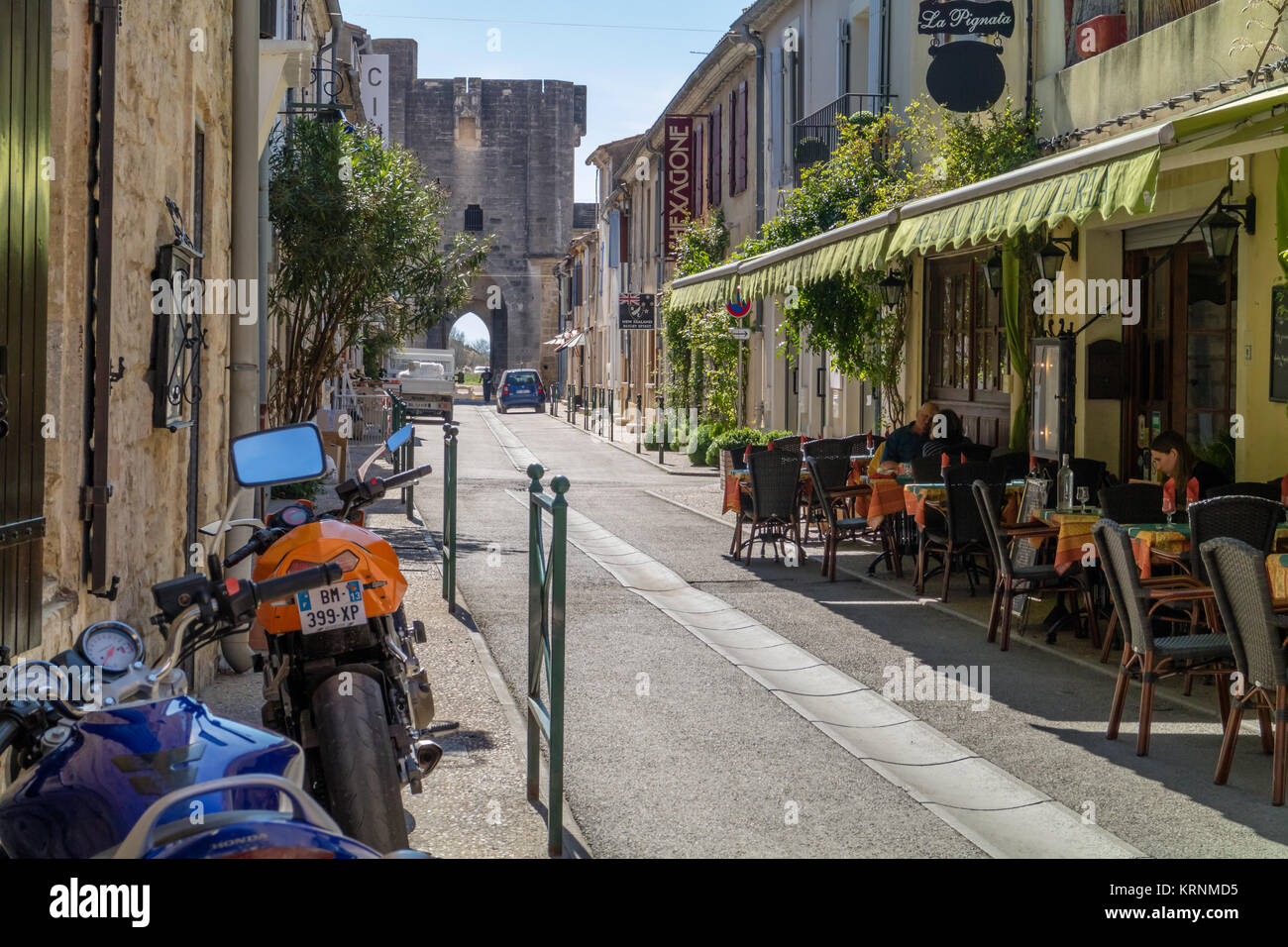 Sonnigen und ruhigen Straße in Aigues-Mortes mit Outdoor Cafe und Turm der Stadtmauer im Hintergrund. Aigues-Mortes, Frankreich. 2017. Stockfoto