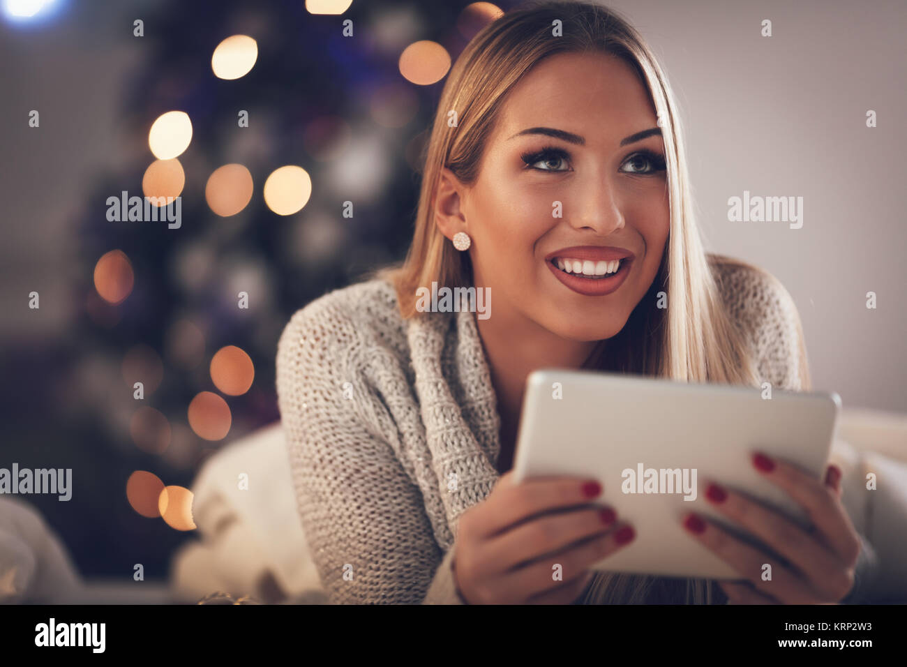 Nette junge lächelnde Frau mit Tablet und nachdenklich Während gemütliche Weihnachten Urlaub zu Hause suchen. Stockfoto