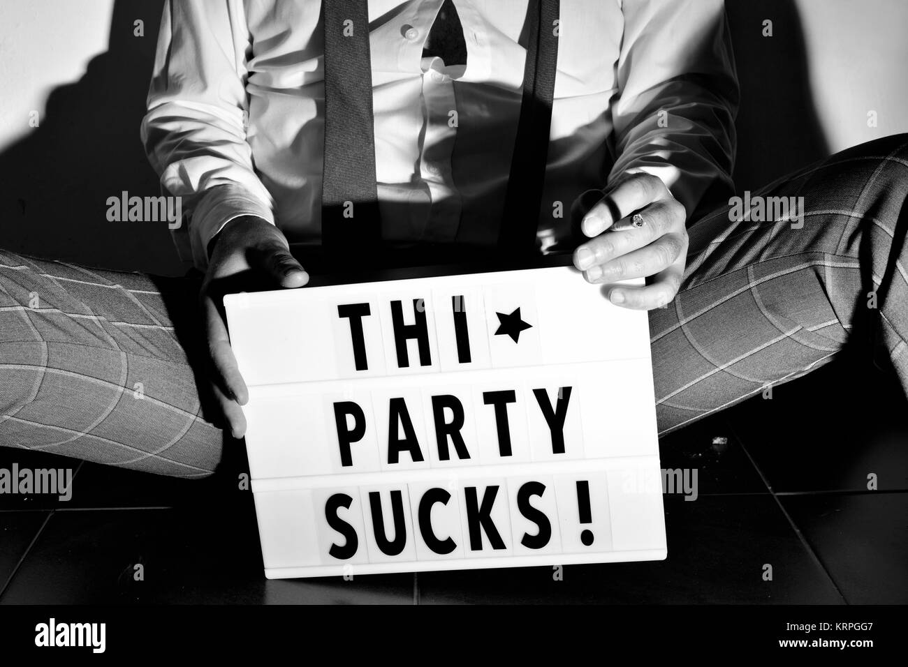 Nahaufnahme von einem jungen Mann sitzen auf dem Boden tragen eine lose Black Tie und rauchen eine Zigarette, und der Text dieser Partei saugt in einer Lightbox neben ihm Stockfoto