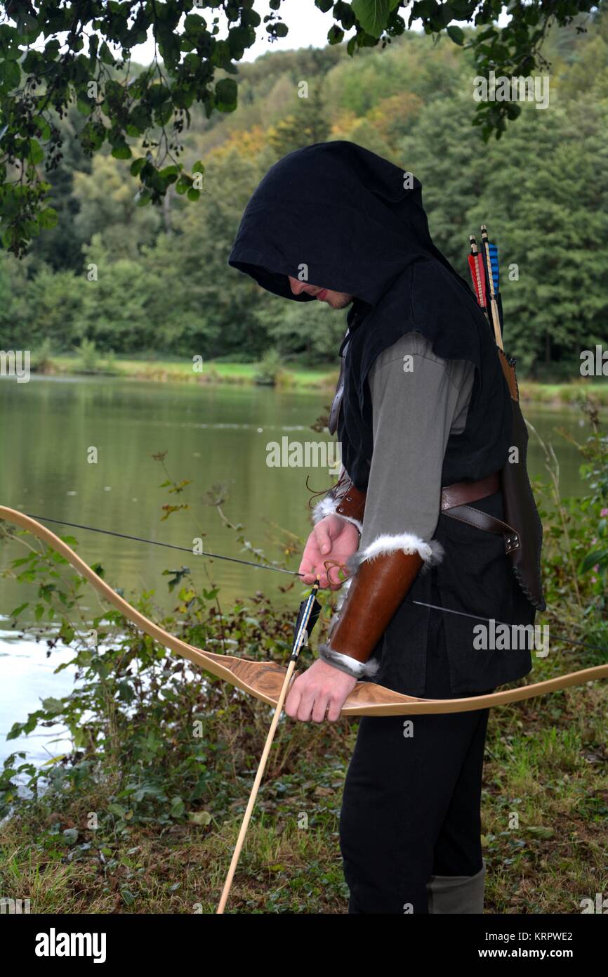 Mittelalterliche Archer mit schwarzer Haube steht mit gespannten Bogen