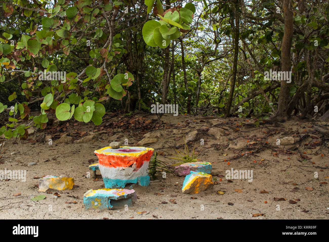 Ein Schleiftisch mit Einrückung und Stein Grinder aus bunt bemalten Stücke aus Beton und Steine am Strand und tropischen Pflanzen in der Stockfoto