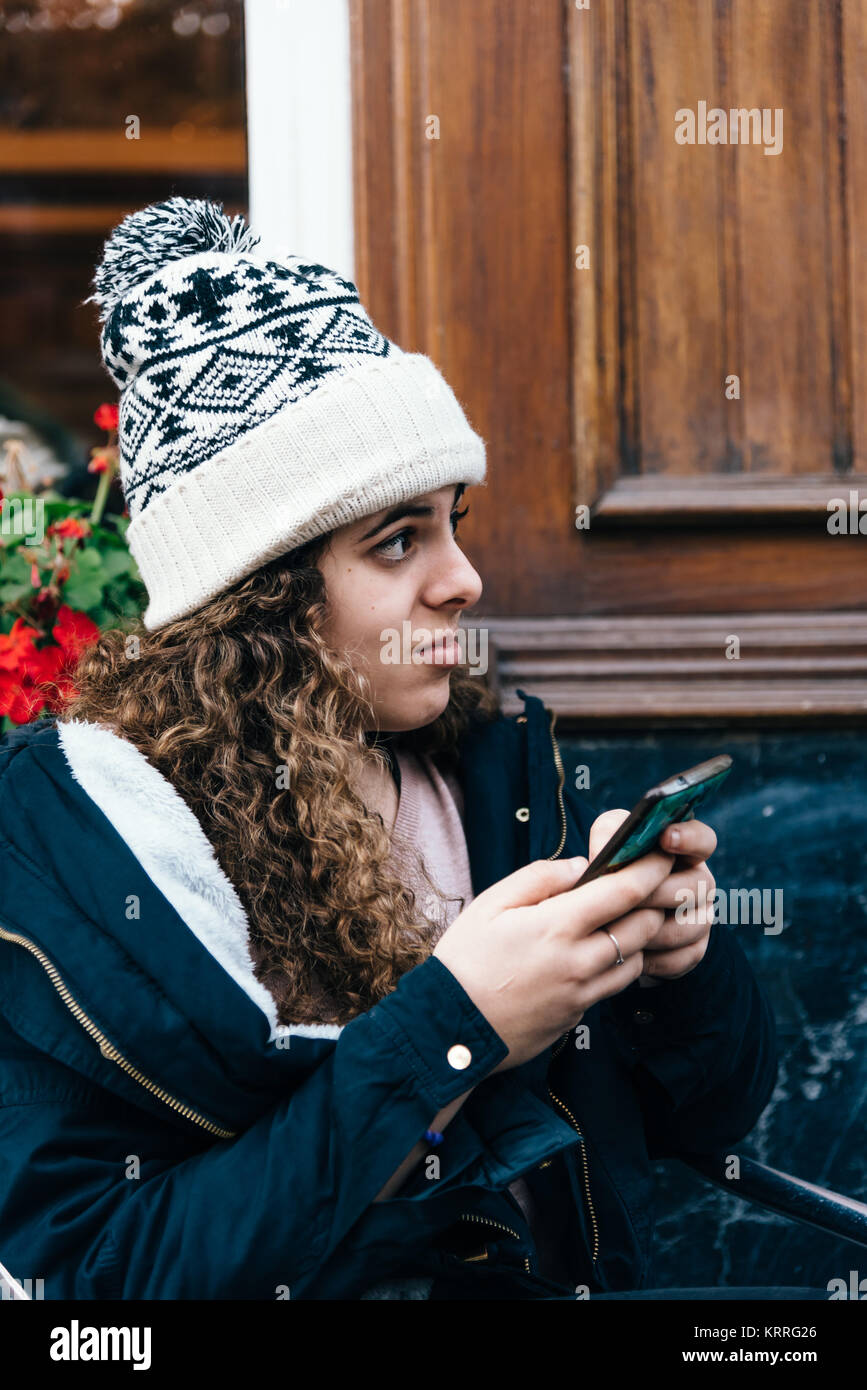 Jugendmädchen in Stricken hat SMS mit Handy Stockfoto