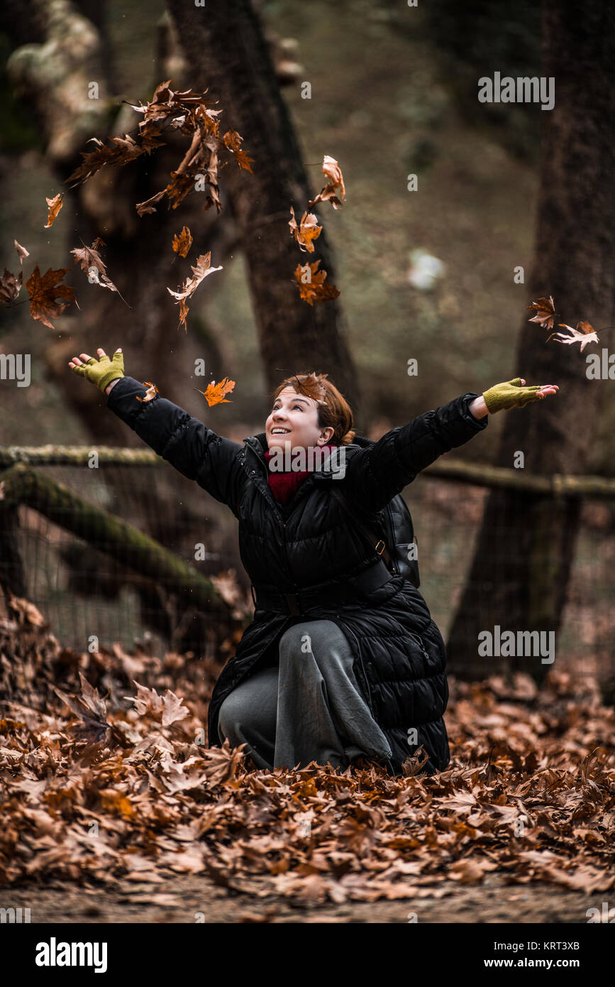 Winter ist gut ... Werfen Blätter in der Luft... Frau mit positiver Energie das Leben genießen und im Herbst im Wald Stockfoto
