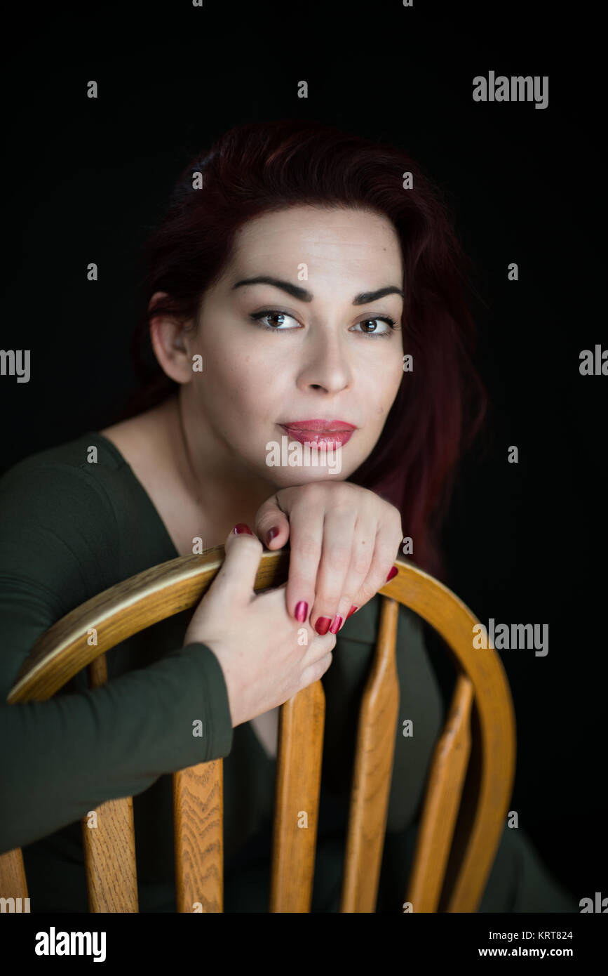 Porträt einer schönen Frau posiert, sitzen auf den Holzstuhl, Studio Shot auf schwarzem Hintergrund Stockfoto