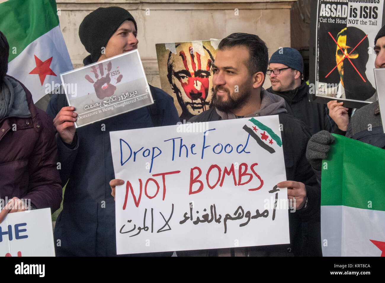 Putin, Assad und eine ISIS balaclava auf Plakaten hinter eine Demonstrantin hält ein Poster 'Drop das Essen nicht Bomben" in Englisch und Arabisch an der Protest für Syrien auf dem Trafalgar Square. Stockfoto